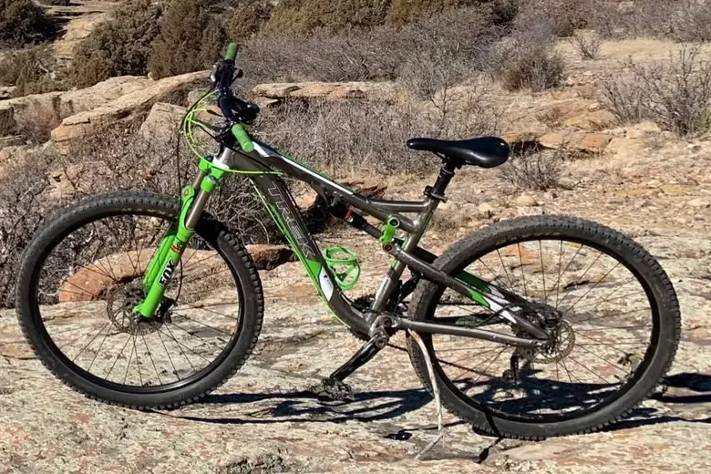 A green and grey Trek full-suspension mountain bike propped on bare sandstone, with dry scrub and rock ledges behind it.